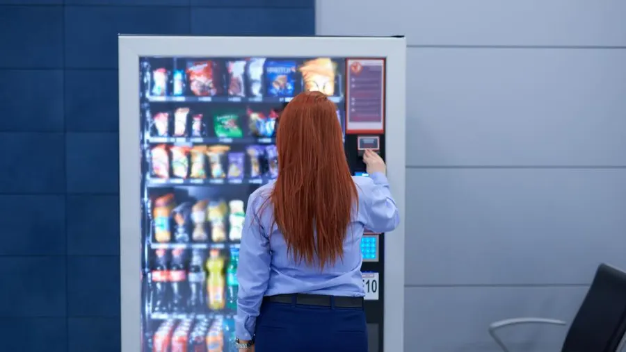 Vending machine business part time UK showing a side hustle operator restocking a machine after work hours with realistic income expectations